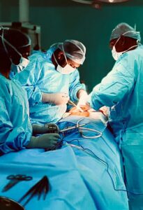 Surgeons in blue scrubs and masks perform surgery around a patient on an operating table with instruments nearby