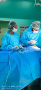 Two surgeons in blue scrubs and masks perform surgery at a sterile operating table.