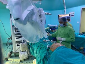 Surgeon in green scrubs and mask operating on a patient with a robotic surgical system in a teal operating room.1