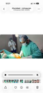 Surgeon in green scrubs and mask performing surgery on a patient; assistant in sterile attire in the background under operating room lights.